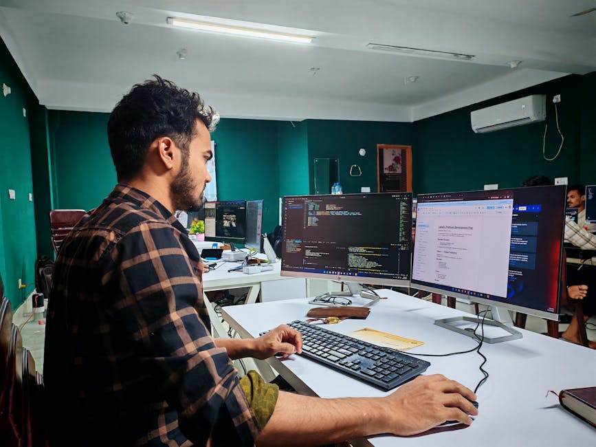Software developer coding on dual monitors in a well-lit modern office