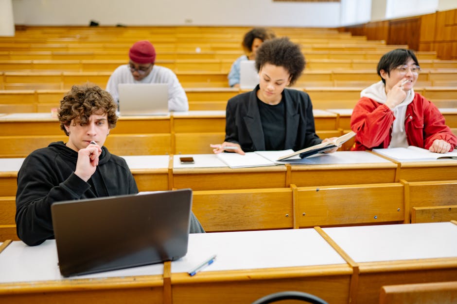 A diverse group of college students studying in a classroom setting with laptops and books